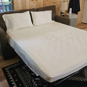 White mattress cover on a sofa bed in a room with wooden walls and a rug.